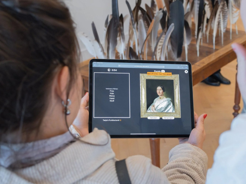 Museum visitor playing Articulate on a tablet, describing a painting